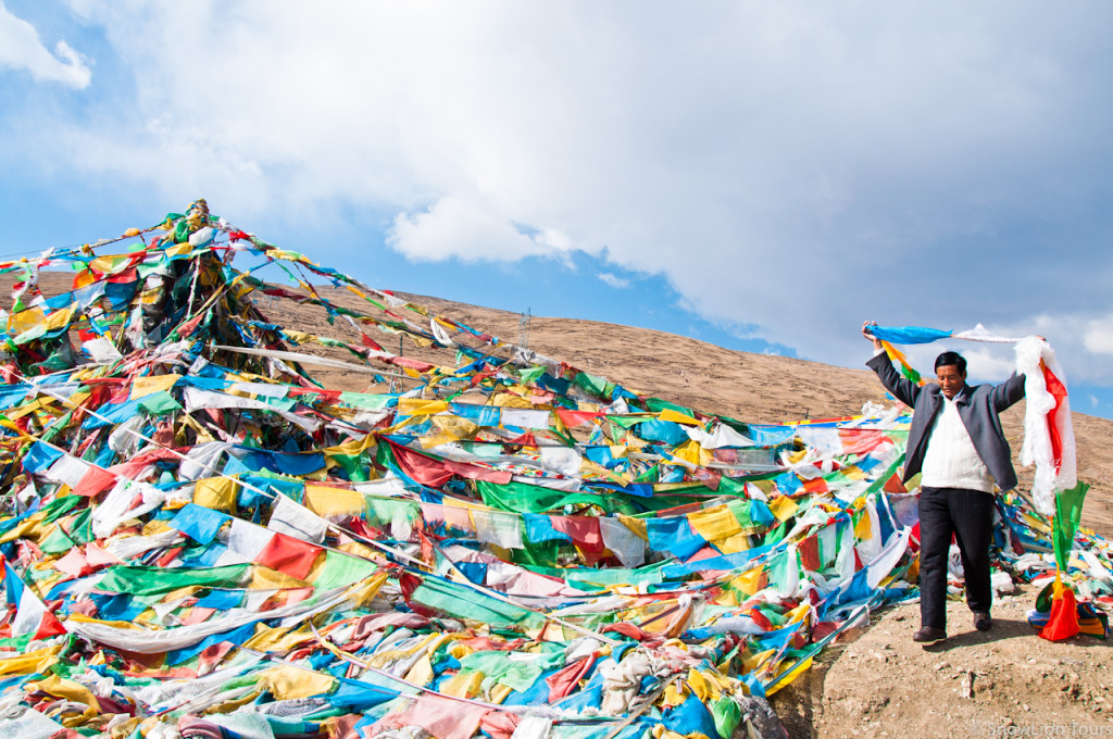 тибетец развешивает молитвенные флажки на перевале после г. Шигатце
